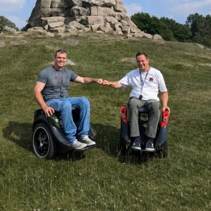 Two smiling men in wheelchairs facing us and giving each other a fist bump.