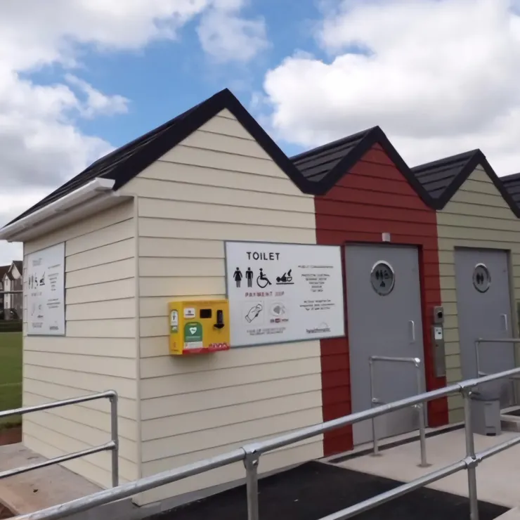 A row of three beach huts that have been made into accessible toilets. The doors are wide, and there is a ramp leading up to them.