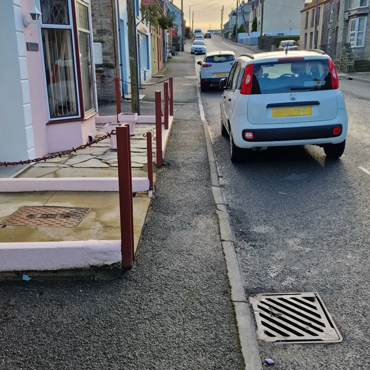 A narrow road with narrow paths either either side of it. There is a pub called the Holly Bush on the left.