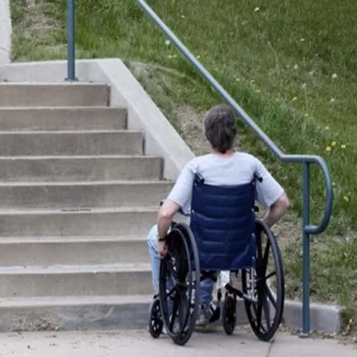 A man in a wheelchair at the bottom of a set of steps, looking up at them. He is facing away from us.